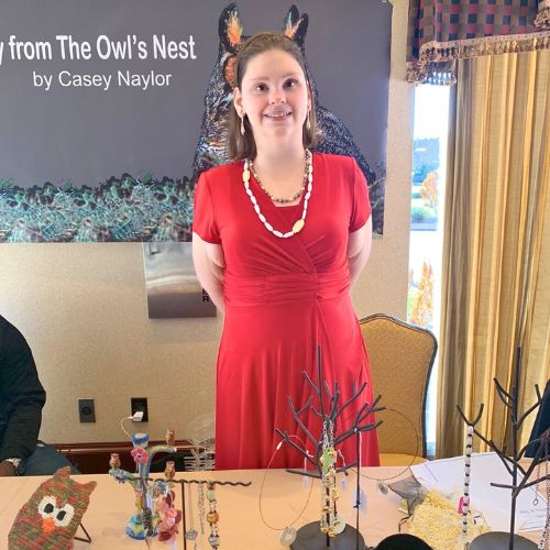 a woman in a red dress is smiling and standing behind a table of jewelry for sale