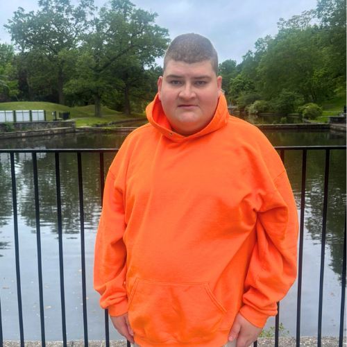 PWS_man-orange-sweatshirt Man in orange sweatshirt standing outside on a bridge over a lake