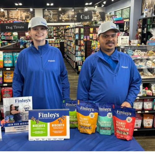 employment program_grocery store two people dressed in matching blue jackets standing in a grocery store at a table with sample products
